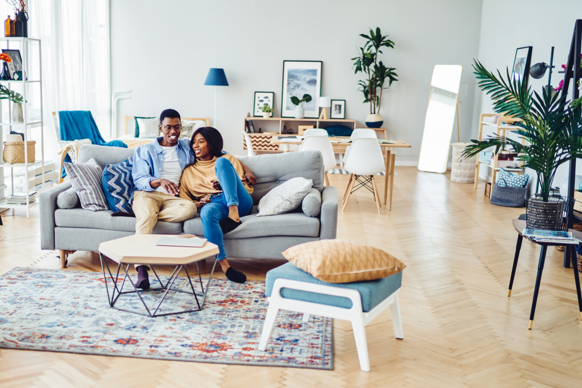 Happy african american young family sitting on sofa in modern designer living room in apartment, positive dark skinned marriage spending time together at home with stylish furniture and decoration
