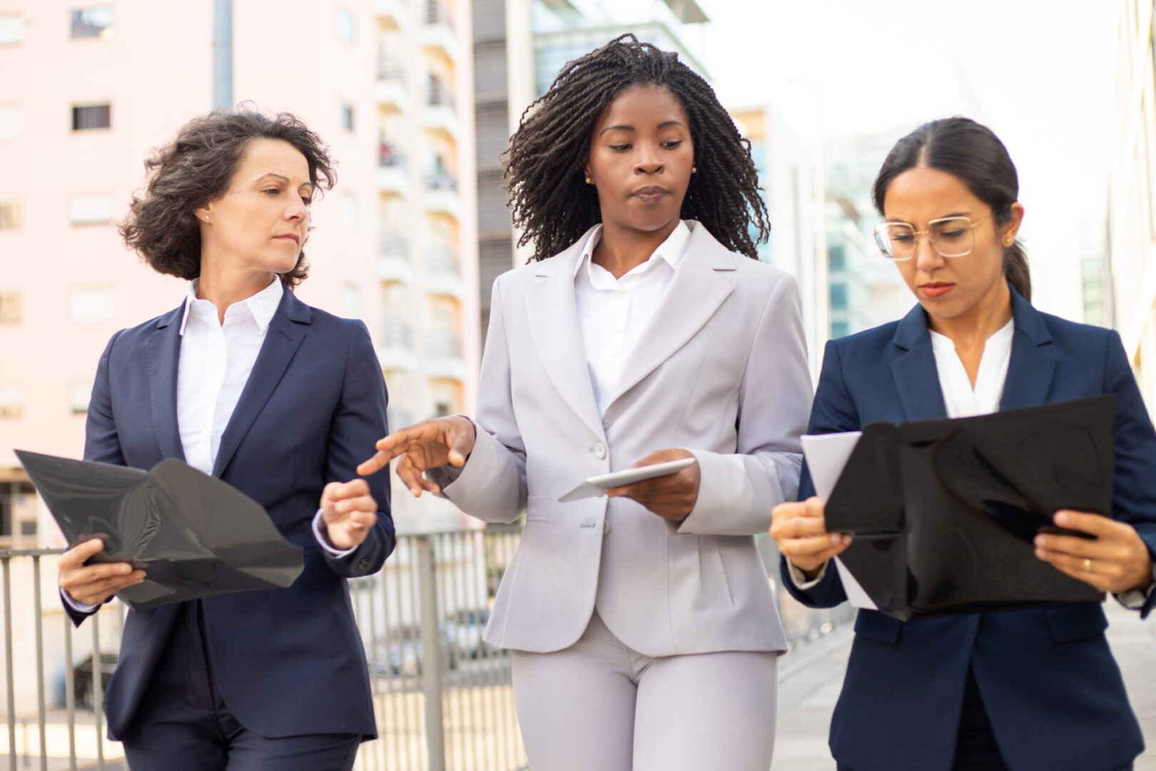 Confident businesswomen discussing documents during stroll. Young female team leader handing out assignments. Colleagues discussing business questions. Teamwork concept